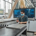 A worker in a mask operates a CNC drill machine on Coated Fiberboard Furniture 11 in an OEM or ODM factory.