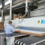 A worker operates a large industrial cutting machine to process Coated Fiberboard Furniture 2 in a factory, showcasing the facility's ODM and OEM manufacturing capabilities.