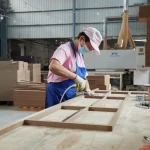 A worker in a mask and apron assembles Coated Fiberboard Furniture 3 at a workbench in an OEM and ODM woodworking factory.