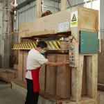 A worker in a mask and red apron operates a large industrial press machine in a factory, producing Coated Fiberboard Furniture 6 for ODM or OEM orders, with material stacks and safety signs visible.