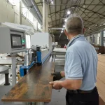 A worker in a light blue shirt operates the Coated Fiberboard Furniture 8, feeding a wooden plank through the machine inside a spacious factory.