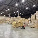 Stacks of Inventory Management 1 boxes are organized on pallets across a spacious, well-lit warehouse. A worker manages operations in this OEM and ODM facility.