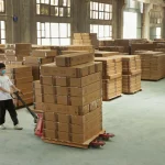 A worker in a mask moves a pallet of boxes inside a spacious warehouse using Inventory Management 3, surrounded by stacks of cardboard boxes.