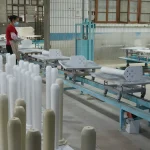 A worker wearing a mask operates at a conveyor belt in an OEM factory, with Wooden furniture 13 arranged in rows.
