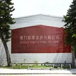 Exterior view of a building with the "Xiamen Toptrue Home Co., Ltd." header and Luxxy branding, shown on a red sign between two trees alongside Chinese characters.