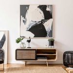 Modern living room with light wooden sideboard, abstract artwork, potted plants, a decorative bird, black basket, and neutral-toned furniture on a woven rug.