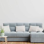 A modern living room featuring the photo-8-2.jpg light blue sectional sofa, white/beige pillows, potted plants, and a side table—ideal for stylishly presenting OEM or ODM furniture solutions.