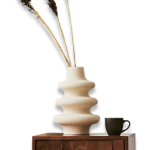 A wavy beige vase with dried plants and a black cup sit on top of the OEM wooden cabinet "photo-9-2.png," which features a textured square pattern.