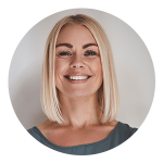 A woman with straight, shoulder-length blonde hair and a blue top smiles at the camera against a plain light background.