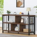 The 01C_结果 wooden and metal console table with open shelves, ideal for ODM/OEM customization, is shown against a white wall decorated with books, a lamp, clock, framed art, plants, a basket, and a bowl of fruit.