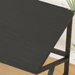 A close-up of the 04.01.C_结果 black textured desk with metal legs, ideal for ODM/OEM, shown on a light wood floor beside a white wall and green plant leaves.