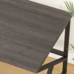 The 04.01.C_结果 OEM desk, featuring a dark wood-grain top and black metal legs, stands on a light wood floor with green plant leaves visible at the edge.