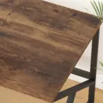 A close-up of the 04.01.C_结果 wooden desk with a dark brown finish and black metal legs. A green plant is partially visible in the upper right corner.