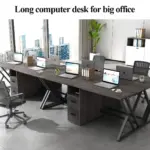 The 04.01.C,jpg_结果 is a long, dark wood OEM computer desk arranged with laptops, monitors, chairs, and office supplies in a modern ODM office with large windows and city views.