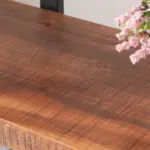 Close-up of the 04.03 Solid Wood Bookshelf’s natural grain tabletop; a glimpse of pink flowers appears in the upper right corner, highlighting the rustic vintage style of this 3-tier industrial open etagere bookcase in distressed brown.