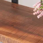 Close-up of the 05.03 HSH Double Wide Solid Wood Bookshelf’s rustic wood surface with visible grain, a black metal frame, and pink flowers in the top right corner.