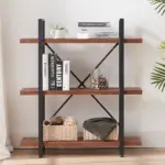 The 07.03 Solid Wood 3-Tier Rustic Vintage Industrial Bookcase features open metal shelving, ideal for OEM/ODM, and displays books, a plant, wicker baskets, a glass jar with pinecones, a blanket, and a mug.