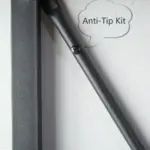 Close-up of a BC02-02 06 - 03 3-Shelf Rustic Industrial Bookshelf's metal anti-tip kit bracket mounted to a wall, with "Anti-Tip Kit" in a speech bubble on the right.