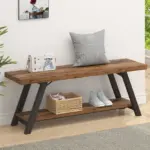 The Industrial Wood Bench in Rustic Brown with black metal legs holds a gray pillow, white bag, and wicker basket with sneakers on the lower shelf, adding a welcoming vibe to the bright entryway.