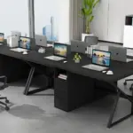 A modern office workspace with six laptops on a large black desk, office chairs, stationery, small plants, and city buildings visible through large windows.