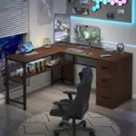 A modern L-shaped desk setup with dual monitors, a keyboard, mouse, laptop, books, car models, and gaming accessories, next to a window overlooking a city at night.