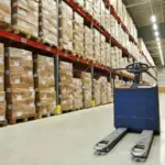 A pallet jack is parked on the floor of a warehouse with tall shelves stacked with boxes and packages, supporting the efficient OEM Service Process.