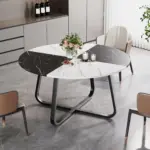 A contemporary dining room features a 42.13-inch round white and black faux marble dining table for 4 to 6, set with flowers, candles, and fruit, surrounded by four chairs.